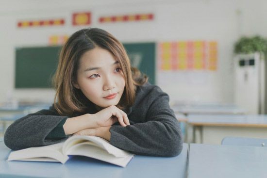 Ein M&auml;dchen mit einem Buch auf dem Tisch, die nachdenklich schaut