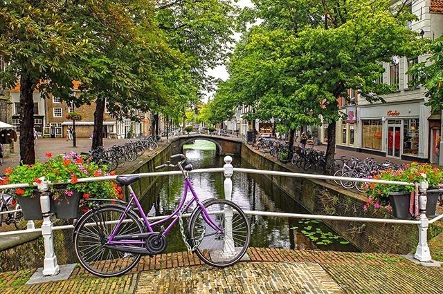 lila Fahrrad in Amsterdam an Br&uuml;ckengel&auml;nder &uuml;ber eine Gracht