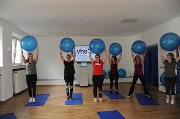 Teilnehmende machen eine &Uuml;bung mit einem Gymnastikball.