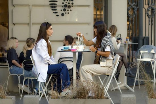 2 Frauen sitzen in einem Caf&eacute; im Freien an einem runden Tisch