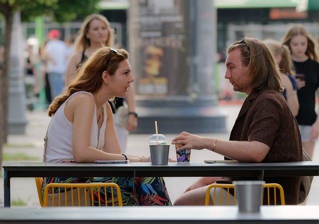 Ein Mann und eine Frau sitzen bei einem Getr&auml;nk in einem Caf&eacute;. Die Frau beugt sich interessiert nach vorn