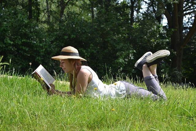 Eine junge Frau mit Strohhut liegt im Gras und liest ein Buch.