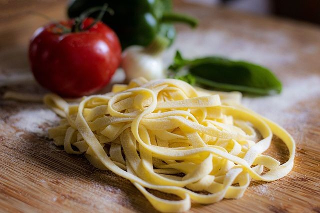 Frische Pasta (Tagliatelle) und eine Tomate und ein Basilikumblatt