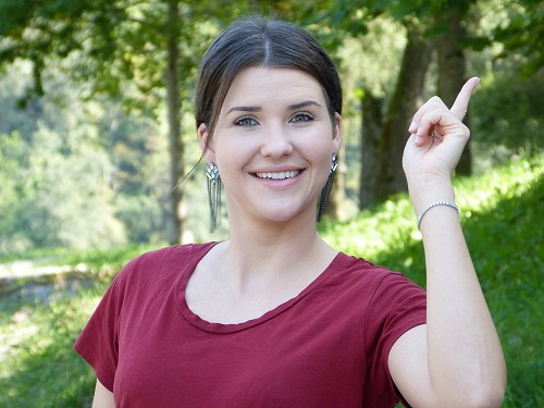 Frau steht im Park und hebt den Zeigefinger