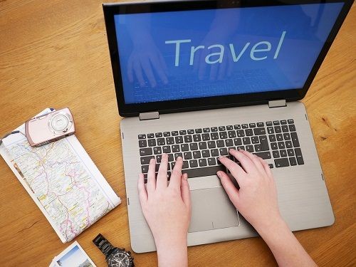 Laptop, Schriftzug Travel, daneben Landkarte und Digitalkamera