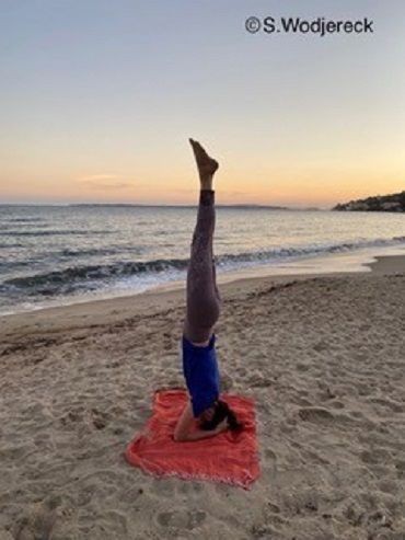 Eine Frau macht am Strand einen Kopfstand.
