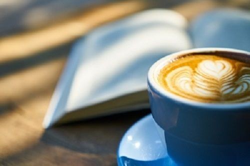 Eine Tasse Cappuccino neben einem aufgeschlagenen Buch im Hintergrund
