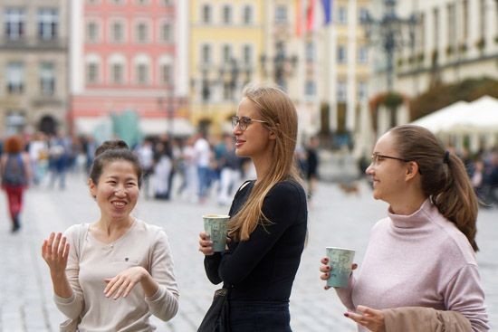 3 junge Frauen stehen in der Stadt auf einem Marktplatz und freuen sich.