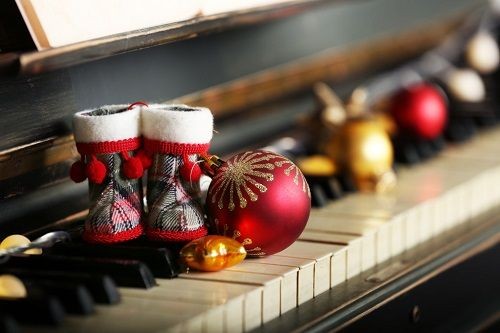 Weihnachtsdekoration auf Klaviertasten: rote Baumkugel und kleine karierte Stiefelchen