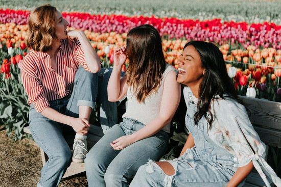 3 junge Frauen sitzen auf einer Bank an einem Tulpenfeld und freuen sich