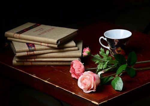 Tisch mit B&uuml;cher, Rosen und einer Tasse
