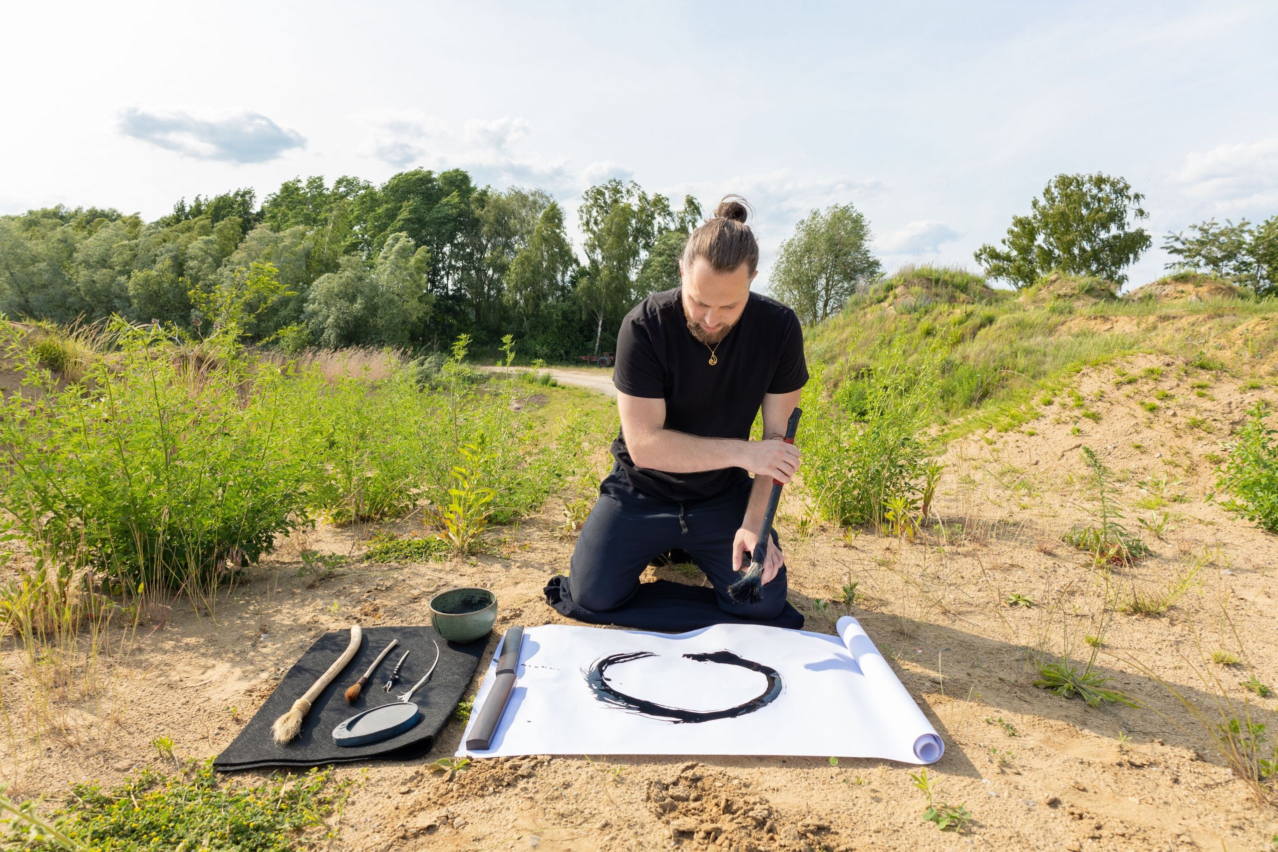 Person kniet in der Natur und schreibt mit einem Naturpinsel