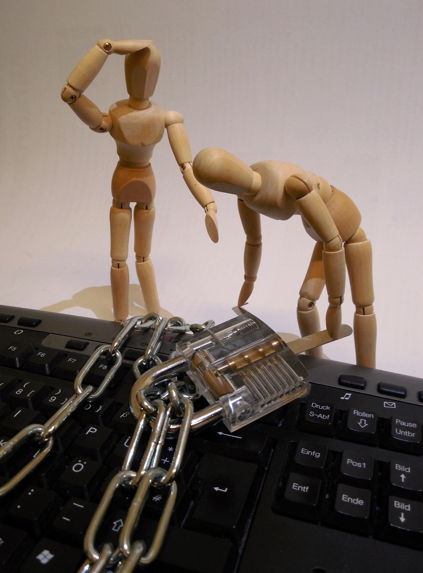 Bild Thema Cybersicherheit - zwei Holzpuppen die ein Schloss um eine Tastatur wickeln