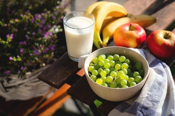 Auf einem Tisch eine Schale mit wei&szlig;en Trauben, &Auml;pfel, Bananen und ein Glas Milch