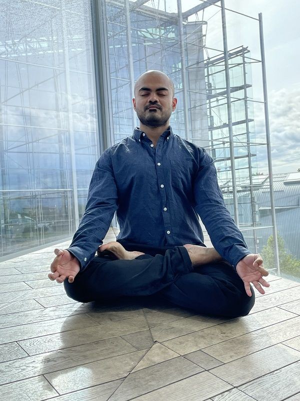 Person im Schneidersitz und Meditationshaltung auf dem Boden in einer Etage eines hohen Geb&auml;udes